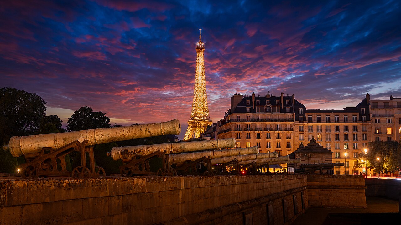 The Eiffel Tower lit at dusk under a red and blue sky in Paris